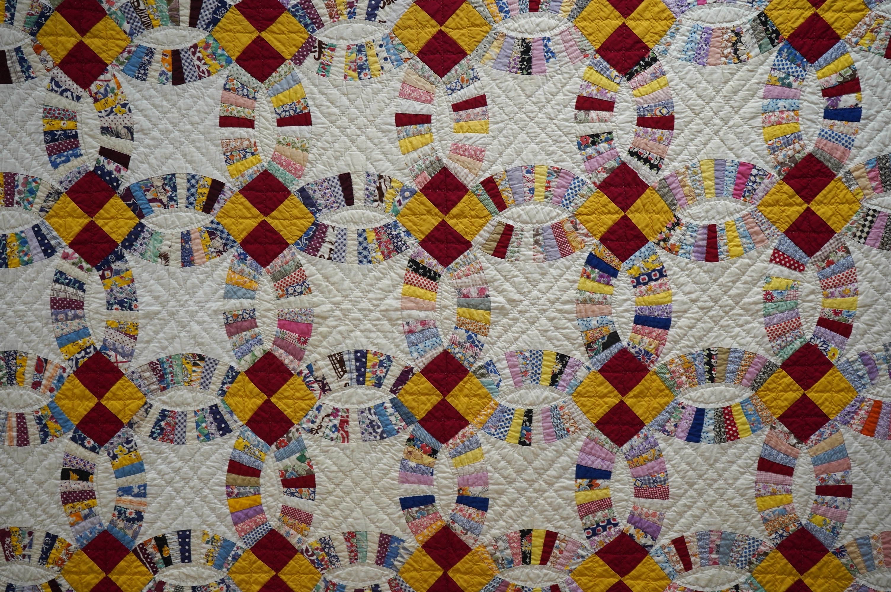 A 1940’s hand made ‘Double Wedding Ring’ patchwork quilt, made from bright multi-coloured floral and plain cotton dress fabrics into a patchwork design of large all over interlocking rings with a scalloped bright yellow